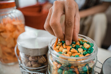 Close up of a hand taking nuts from a glass jar full of snacks on the table in the living room