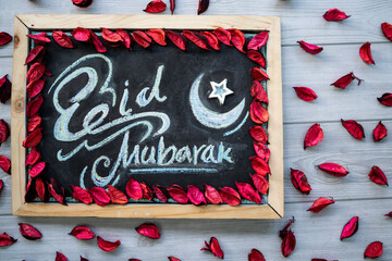 Eid Mubarak English Calligraphy image, Eid Mubarak greetings on black board with rose petals