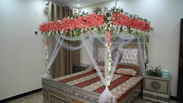 Honeymoon suite with canopy bed, free space. Luxurious wood canopy bed with flowers and pillows on it. Female bedroom in pink and white colors, copy space. Big comfortable bed in elegant bedroom