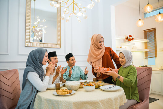 group of Muslim friends clapping happily when one of their friends is given a surprise gift at the dinner table