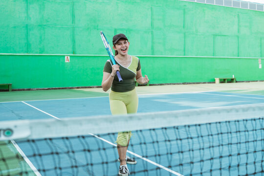 female tennis player shouting happily with fists clenched while scoring points on tennis court