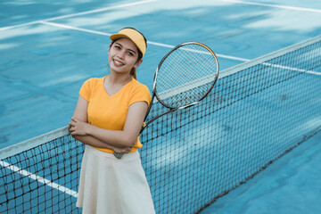 Beautiful female tennis player standing with crossed hands holding racket on tennis court