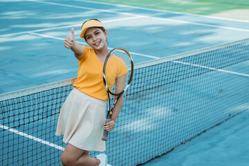 Beautiful tennis player woman standing with thumbs up while holding racket on tennis court