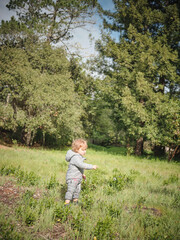 A toddler in a grey snow suit plays in a field after a rainstorm