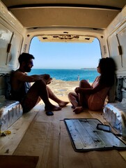 Relaxing couple seated inside the back of a van in front of the ocean.