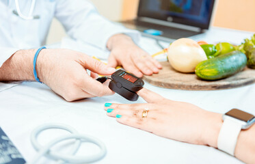 Close up of hands of nutritionist using pulse oximeter on patient finger.  Nutritionist measuring...