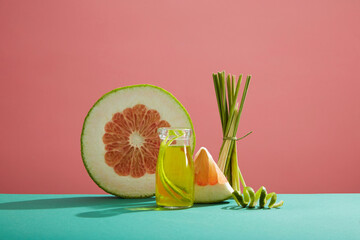 Front view of glass bottle, fresh lemongrass, slices of pink pomelo and pomelo peel on pink...