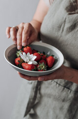 A gray plate with strawberries and flower in women's hands.