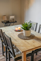 Top view of wooden dining table with chairs and decorative elements plant, candles, pillows on a light wall background. Concept of stylish interior and natural materials in the decor