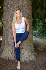 Pretty healthy blond woman posing against a tree trunk