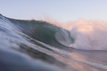 huge wave breaking on a shallow reef in golden morning light, copy space and no people