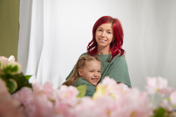 Amazing pretty mother and daughter having fun with flowers in 8 March or in Mother's day. Red haired mom and small little blonde girl having lovely free time on white background