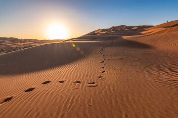 Footprints in sand dunes of Abu Dhabi desert at sunset. - obrazy, fototapety, plakaty