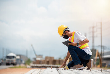Asian engineer wearing hard hat and safety vest sitting and checking construction problems in...