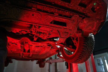 the bottom of the car lifted on a car lift in the workshop. you can see the wheel, engine...