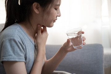 Young Asian woman have a sore throat cough symptom and feel sick from virus or bacteria infection influenza by touching her neck and hard to swallow and drink water