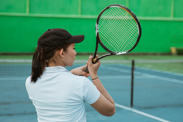 back of the shoulder of a female tennis athlete holding a racket hitting the ball on the court