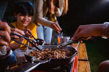 Fototapeta premium the group of people grilling the beef and the onions using the grilled pan and portable stove at the camp site