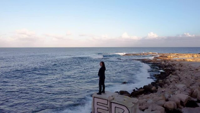 Drone shot view of a girl standing on the edge of part of abandoned Jerma Palace Hotel in Malta