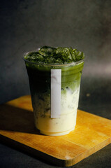 Close up of matcha latte juice in plastic glass with white sticker tag on wooden plate with gray background