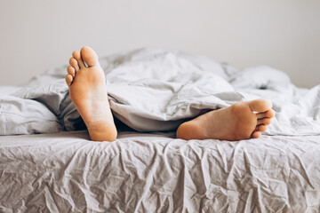 Young man sleeping in bed at home with focus on legs. Feet of man lying in the bed