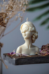 Beautiful handmade candle in the shape of a female body on a wooden stand surrounded by flower petals