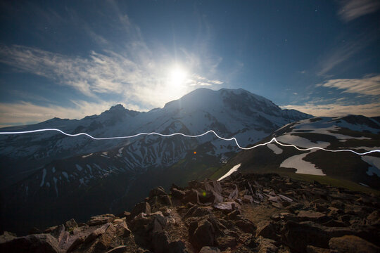 A hiker's healamp trail crosses  Burroughs Mountain while the Moon rises over Mount Ranier.