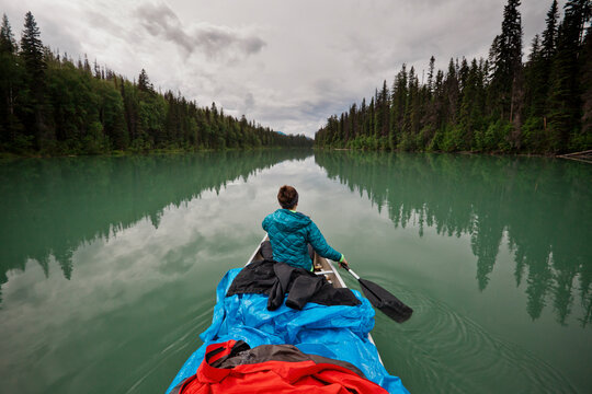 A woman paddles her canoe while rain jackets lay out to dry during a multi-day canoe trip
