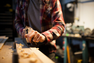 A carpenter works on a piece of wood with a hand planer.