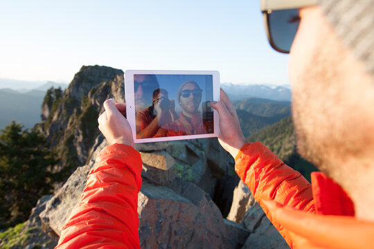 A hiker uses a tablet to take a selfie of himself and his friend.