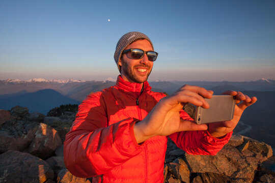 A hiker uses his smartphone to take a a picture of the view from the summit of Sauk Mountain, Washington.