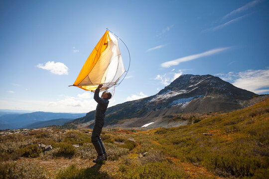 A Hiker Shakes Out His Tent Below Jim Kelly Peak In Illal Meadows