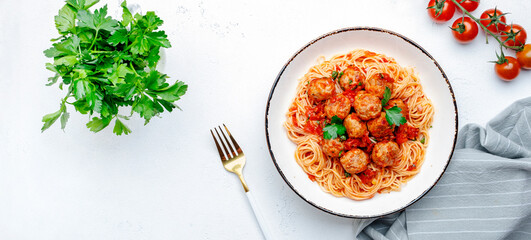 Spaghetti pasta with meatballs in spicy tomato sauce with parsley in plate, white table background,...