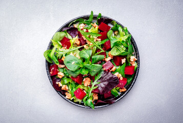 Beet and herbs healthy salad with arugula, lamb lettuce, mini chard and walnuts, gray kitchen table, place for text. Fresh useful vegan dish for healthy eating