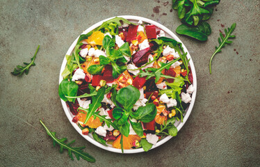 Beet, soft cheese and orange healthy salad with arugula, lamb lettuce, mini chard and pistachios, rusty green kitchen table.. Fresh useful dish for healthy eating