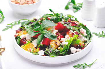 Beet, cheese and orange healthy salad with arugula, lamb lettuce, mini chard and pistachios, white kitchen table, copy space.. Fresh useful dish for healthy eating