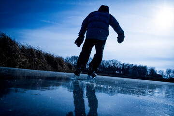 Low angle perspective of a young boy out skating on the frozen lake along an island of reeds.