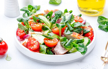 Fresh salad with grilled chicken slice with red tomato, cucumber, red onion, lamb lettuce and sesame seeds on white table background, top view