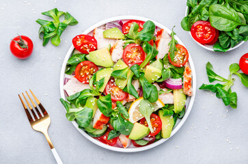 Chicken salad with red tomato,  avocado, cucumber, red onion, lamb lettuce and sesame seeds on gray table background, top view