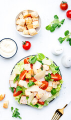 Caesar salad with chicken, iceberg salad, croutons, parmesan cheese and tomatoes with caesar dressing. White table background, top view