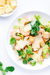 Caesar salad with shrimp, iceberg and lamb lettuce, croutons, parmesan cheese with caesar dressing. White table background, top view