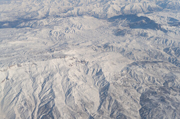 Fototapeta premium Wing of aerial view of an airplane jet flying above clouds from the window in traveling and transportation concept. White snow mountain in winter season. Nature landscape background.