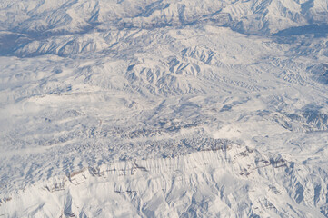 Wing of aerial view of an airplane jet flying above clouds from the window in traveling and transportation concept. White snow mountain in winter season. Nature landscape background.