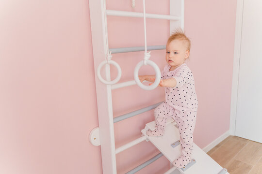 A Caucasian girl in soft pink pajamas does sport at gymnastic rings