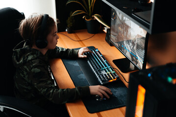 Young gamer boy with headphones playing computer video game. © stenkovlad