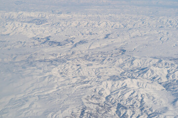 Wing of aerial view of an airplane jet flying above clouds from the window in traveling and transportation concept. White snow mountain in winter season. Nature landscape background.