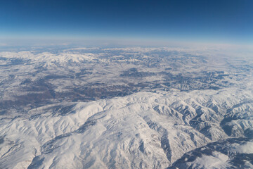 Wing of aerial view of an airplane jet flying above clouds from the window in traveling and transportation concept. White snow mountain in winter season. Nature landscape background.