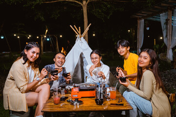 a group of people smiling and eating the grilled beef together at the camp site