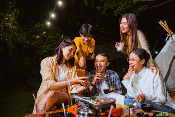 woman in orange stripped shirt holding the phone and showing it to her friends at the camp site