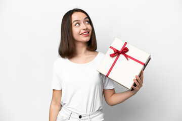 Young Ukrainian woman holding a gift isolated on white background looking up while smiling